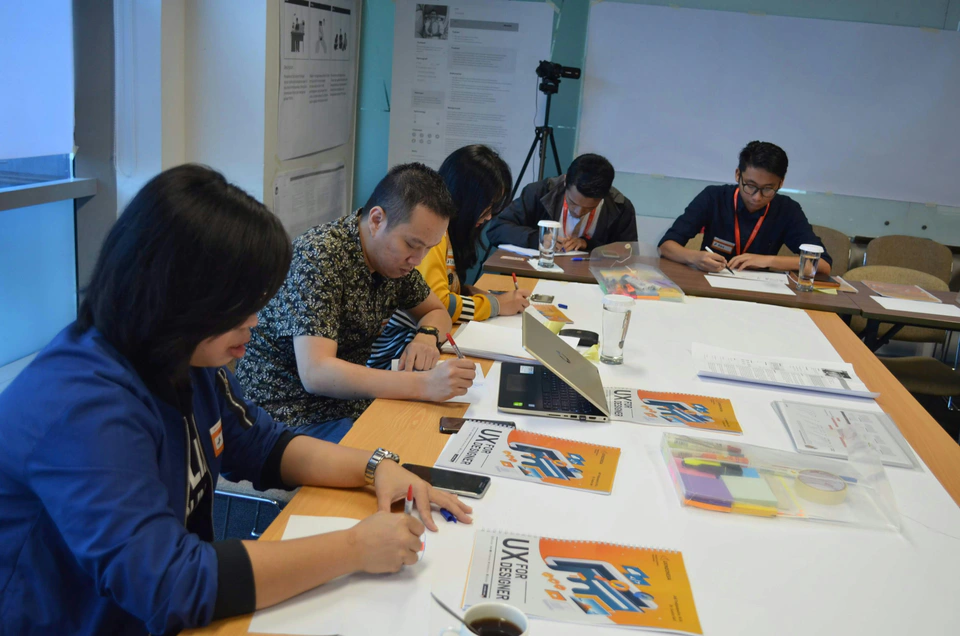 An Indonesian workshop team sketching and reviewing ideas around a table.