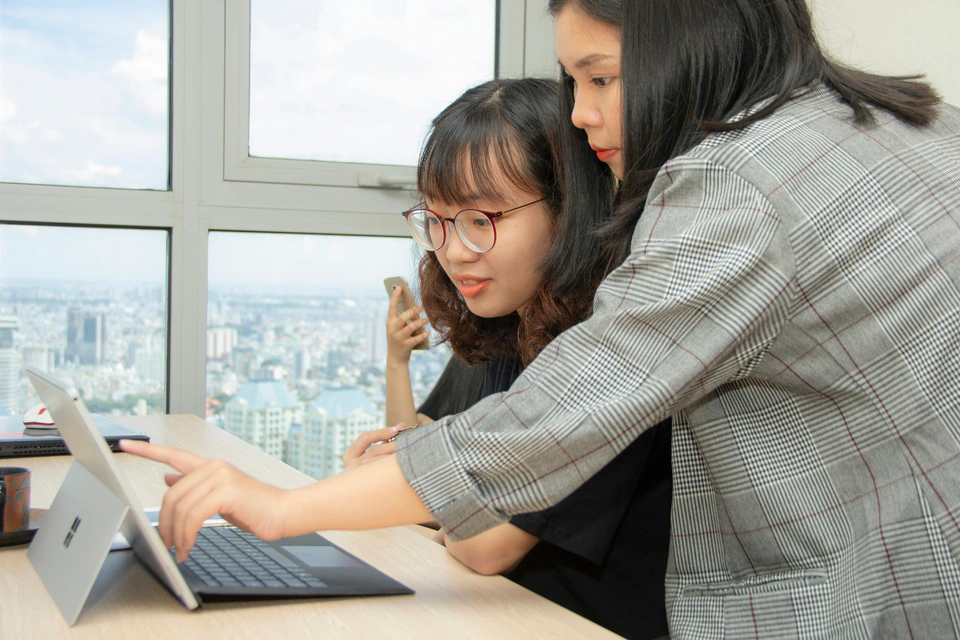 Two colleagues helping each other with a laptop in a Vietnamese agency.